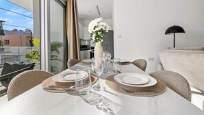 Ein Esstisch ist gedeckt mit Tellern, Gläsern und einer Blumenvase in einer modernen Wohnung mit Balkonblick.