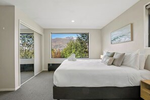 Ein Schlafzimmer mit großem Fenster, einem Bett, einem Nachttisch und einem Bild an der Wand.