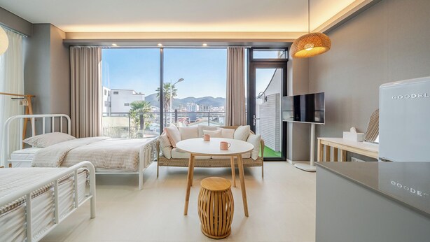 Quarto de hotel com cama, sofá, mesinha, televisão e vista para a cidade.