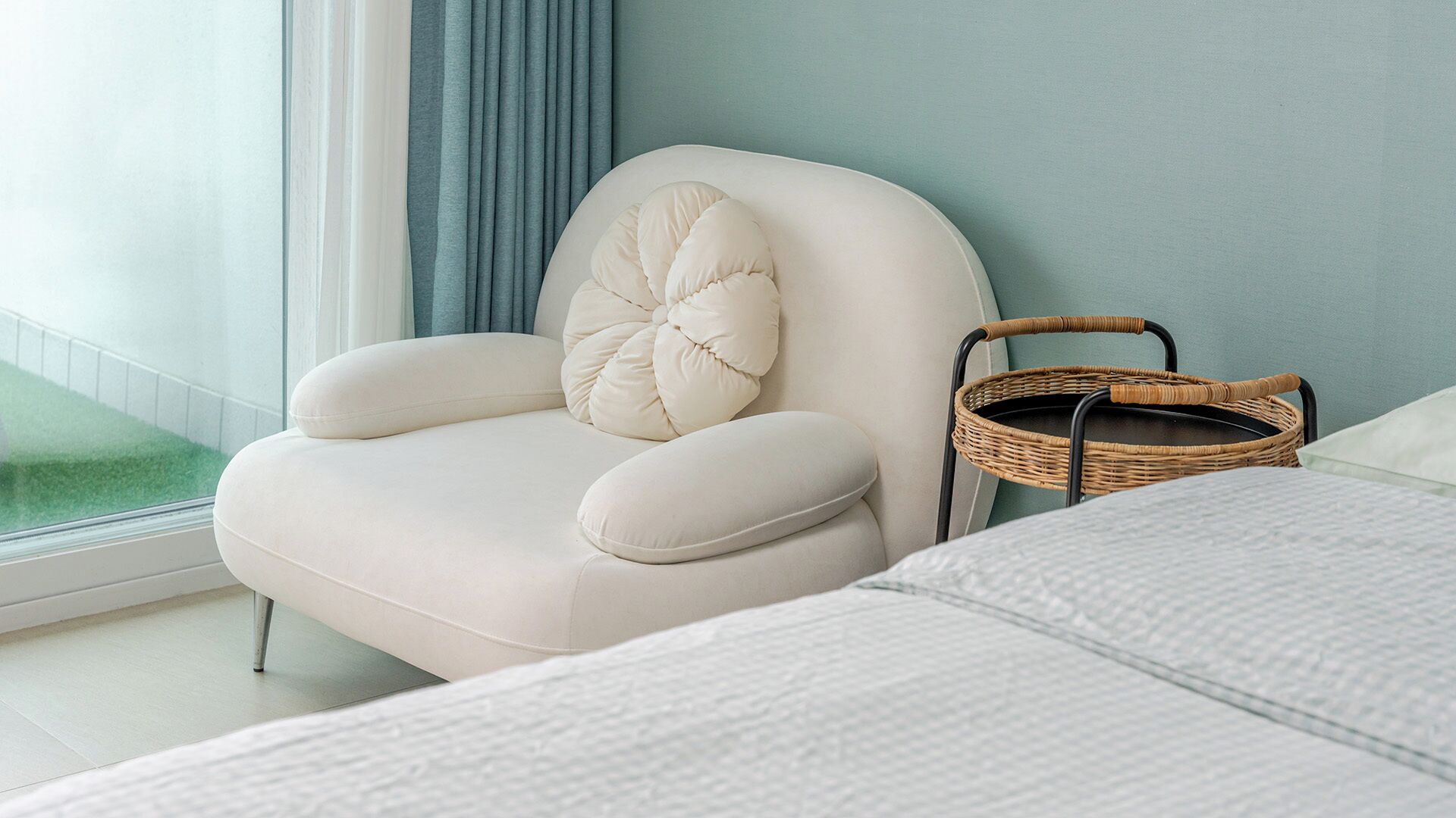 A bedroom with a white chair, a wicker basket, and a bed with white bedding.