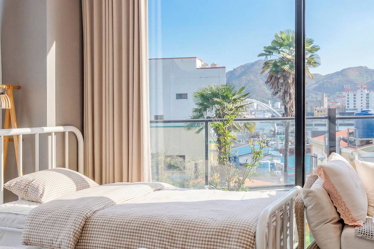 Una habitación de hotel con cama, una silla y ventana con vistas a edificios y montañas.