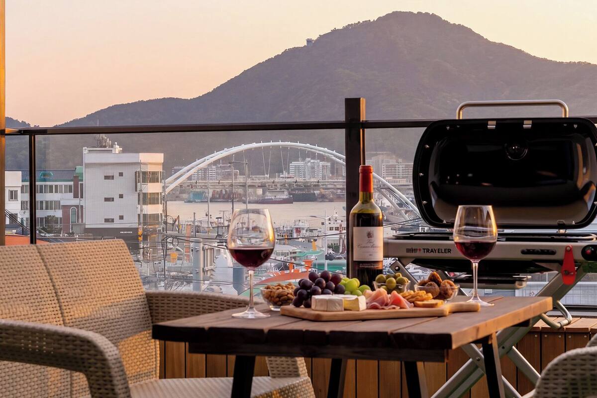 Un balcón con mesa dispuesta para una comida, una botella de vino y una parrilla.