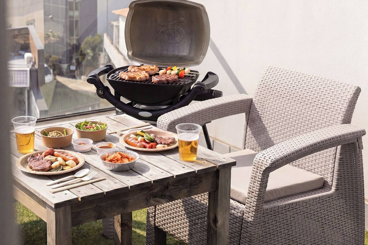 Un patio con una parrilla, mesa de comedor, sillas de mimbre y diversos platos y bebidas.