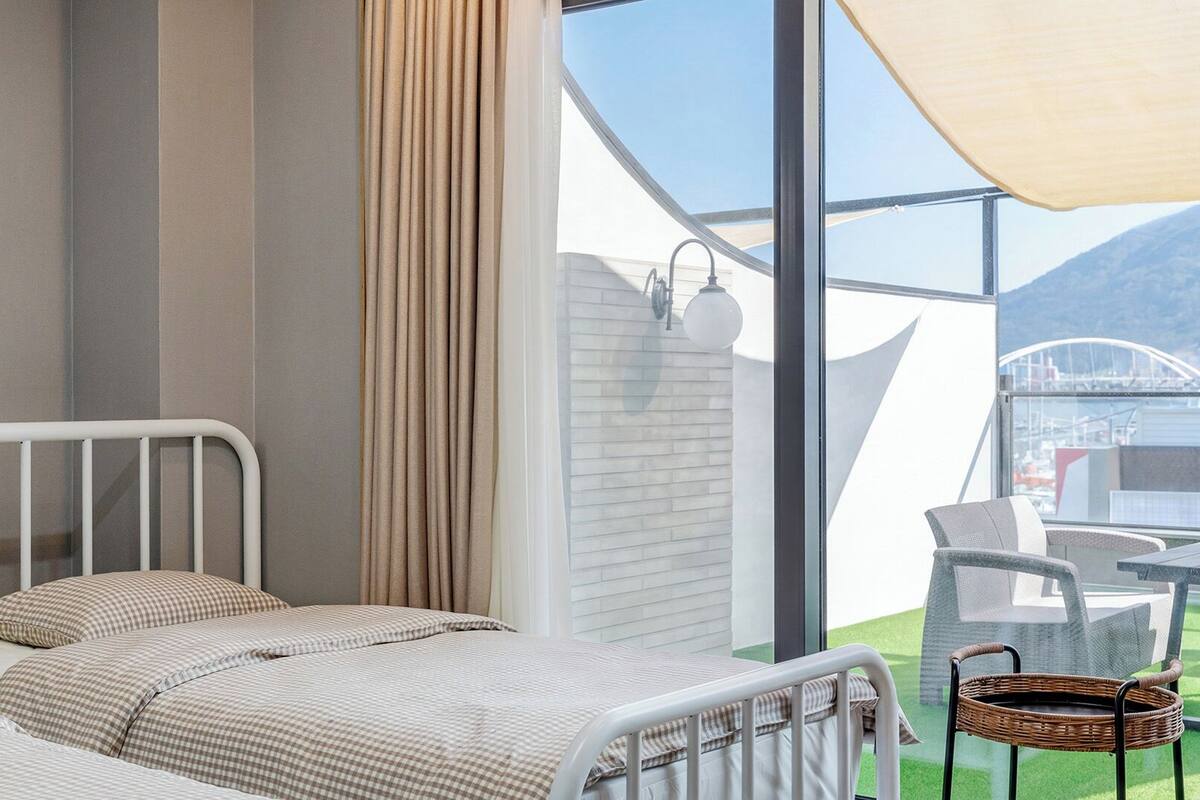 Un dormitorio con cama, cortinas y vistas a un balcón con mobiliario exterior.