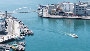 Un paysage urbain côtier avec un pont imposant, une marina où sont amarrés différents bateaux et un hôtel offrant une vue sur l’eau.
