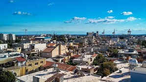 Un paisaje urbano con una combinación de edificios residenciales y comerciales, un cielo azul despejado y grúas a lo lejos que señalan actividad de construcción.