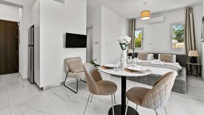 Una habitación de hotel moderna con comedor, sofá, televisor y ventana con cortinas.