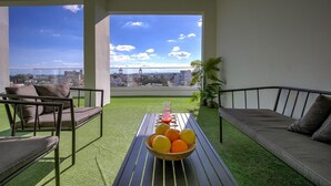 Ein Balkon mit Blick auf die Stadt, eine Couch, ein Sessel und ein Tisch mit Früchten.