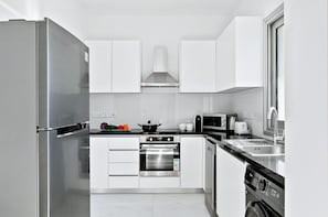 A modern kitchen with stainless steel appliances, white cabinetry, and a black countertop.