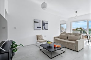 A modern living room with a sofa, a coffee table with fruit and drinks, a chair, and artwork on the wall.
