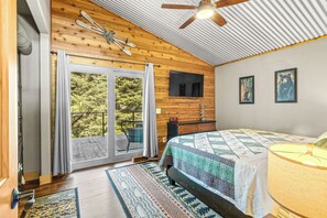 Un dormitorio con cama, ventilador de techo, televisión y vista a un espacio exterior por medio de una puerta corredera.