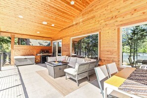 Un espacio al aire libre techado con techo de madera, mobiliario de mimbre, una parrilla y ventanas amplias.