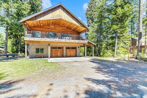Une cabane en rondins à deux étages, dotée d’une grande terrasse, d’un garage et de fondations en pierre.