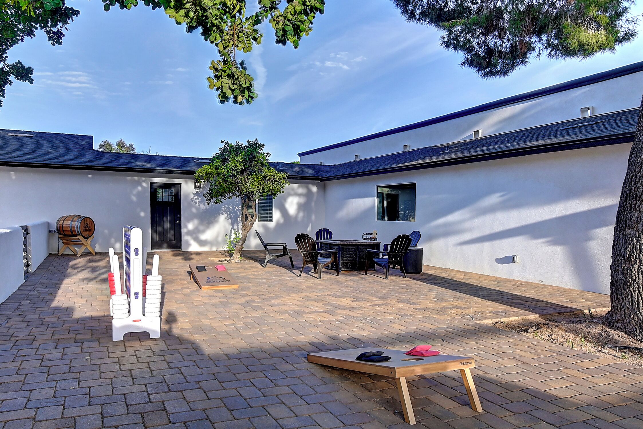 Une cour avec une table et des chaises, un banc en bois et une structure blanche.