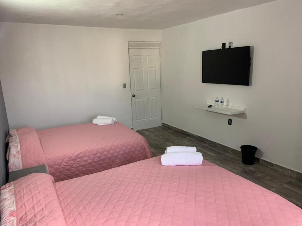 A room with two beds, a TV mounted on the wall, a small shelf with toiletries, and a door.