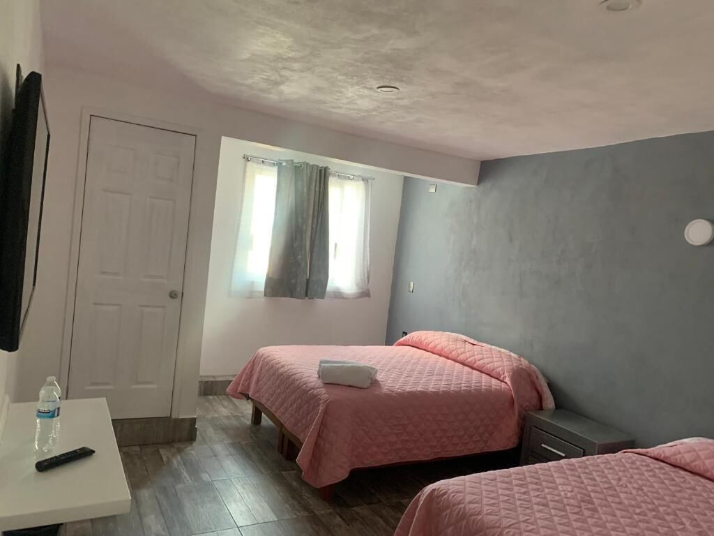 A bedroom with two beds, a white desk, a window with curtains, and a door.