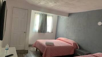 A bedroom with two beds, a white desk, a window with curtains, and a door.