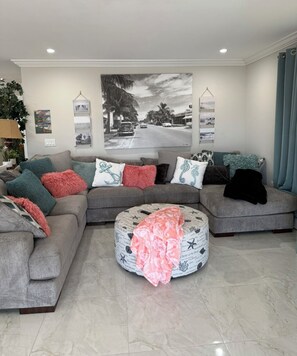 Ein Wohnzimmer mit einem Ecksofa, einem Hocker und einem großen Wandbild.