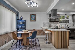 A modern kitchen with a central island, bar stools, and a dining area with chairs. - Serene 2BR Valley Glen Oasis: Private Yard, & BBQ (Los Angeles)
