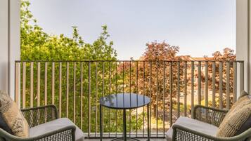 A balcony with two wicker chairs and a small round table, overlooking a residential area with trees and houses.
