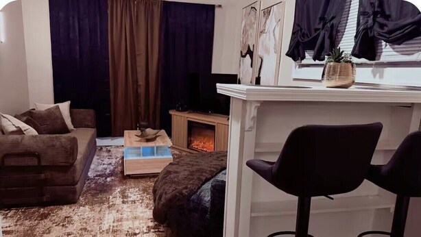 Una sala de estar con sofá, mesa de centro, chimenea, televisor y zona de bar con una silla.