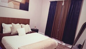 Un dormitorio con cama, mesita de noche y un amplio ventanal con cortinas.