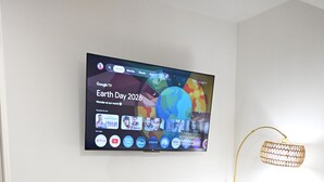En moderne stue med et fladskærms-tv monteret på væggen, et hvidt tv-møbel, en gulvtæppe med sort og gule mønstre og en gulvlampe.