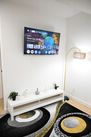 Uma sala de estar moderna com uma TV de tela plana na parede, um rack branco, um tapete com padrão preto e amarelo e um abajur.