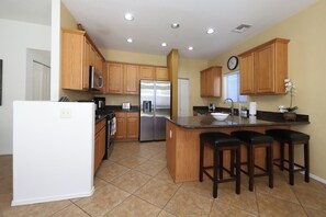 A kitchen with wooden cabinets, a stainless steel refrigerator, a sink, and a clock on the wall. - Spacious 4-bedroom house with office and loft in fabulous Tucson. (Tucson)