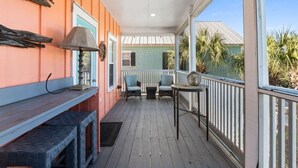 Eine überdachte Veranda mit Holzboden, zwei Stühle, einem kleinen Tisch und einer Lampe.