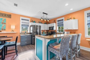 A kitchen with white cabinets, a central island, bar stools, and a dining table. - Cozy Bay-View 2BR/2.5 Bath in Port St. Joe with Pool & Beach (Port St. Joe)