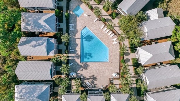 Eine Vogelperspektive zeigt ein Hotel mit mehreren Gebäuden, einem zentralen Schwimmbecken und umliegenden Palmen.