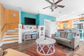 A living room with a sofa, a coffee table, a TV, and a staircase. - Cozy Bay-View 2BR/2.5 Bath in Port St. Joe with Pool & Beach (Port St. Joe)