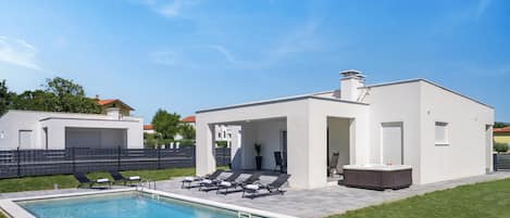 A modern outdoor pool area with lounge chairs and a hot tub.