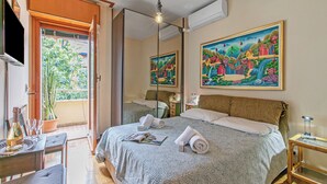 Hotellihuone, jossa on sänky, pöytä, jonka päällä on pullo ja laseja, peili ja taulu seinällä.