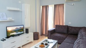 Una sala de estar moderna con un televisor de pantalla plana, un sofá, una mesa de centro con una bandeja de muffins y un armario blanco.