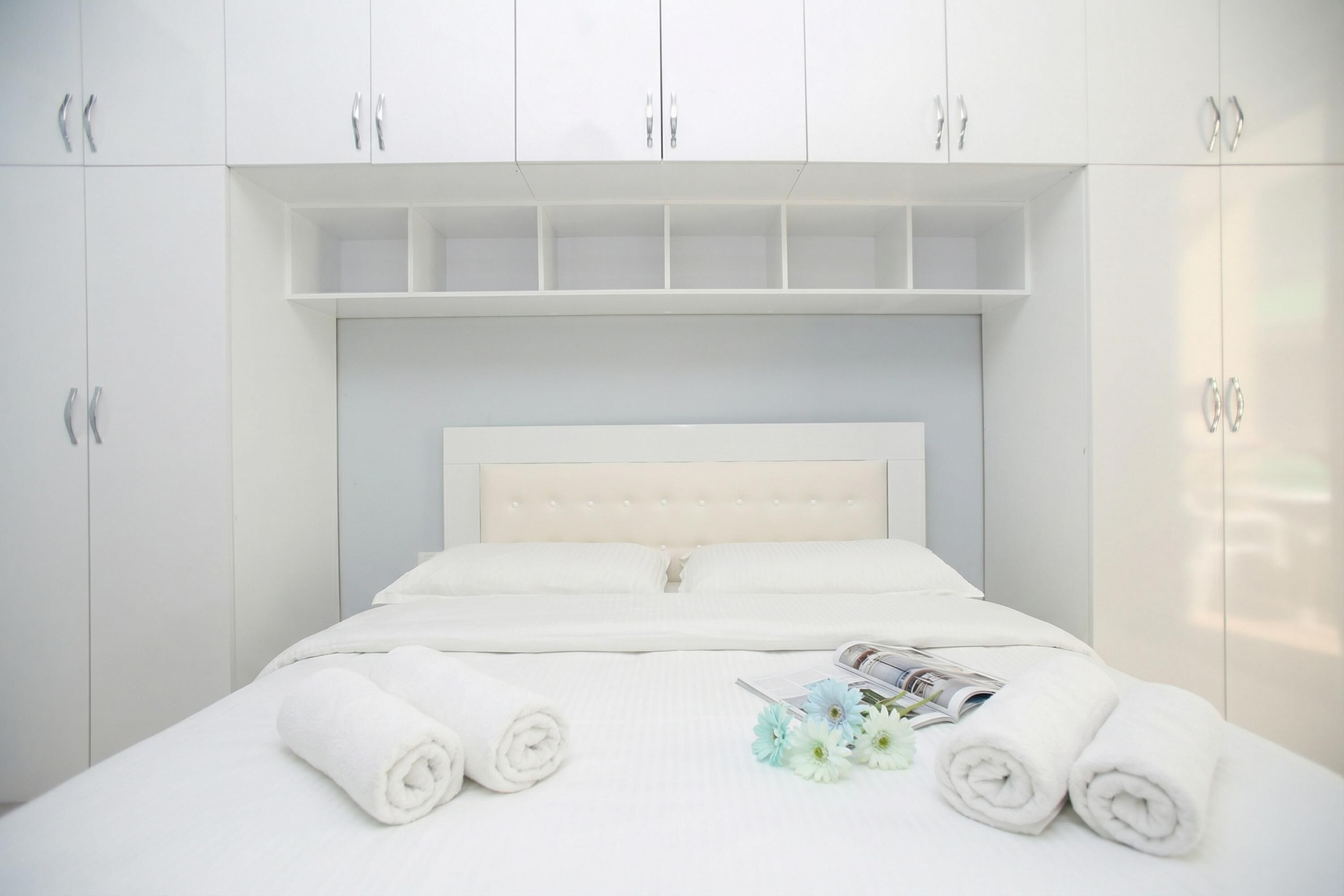 A neatly made bed with white linens and rolled towels, a magazine, and a bouquet of flowers on the bed.