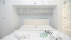 Una cama bien hecha con sábanas blancas y toallas enrolladas, una revista y un ramo de flores sobre la cama.