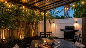 An outdoor patio with a table set for dining, surrounded by chairs, a grill, and string lights. - Luxury Pool Oasis • 5 Min to Beach • Modern Retreat (Hallandale Beach)