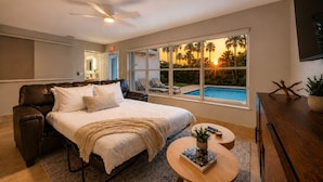 A bedroom with a bed, a ceiling fan, a large window with a pool view, and a TV. - Luxury Pool Oasis • 5 Min to Beach • Modern Retreat (Hallandale Beach)