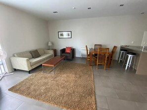 Ein Wohnzimmer mit einer Couch, einem Couchtisch, einem Esstisch mit Stühlen und einer Küchenzeile mit einer Arbeitsfläche und Hockern.