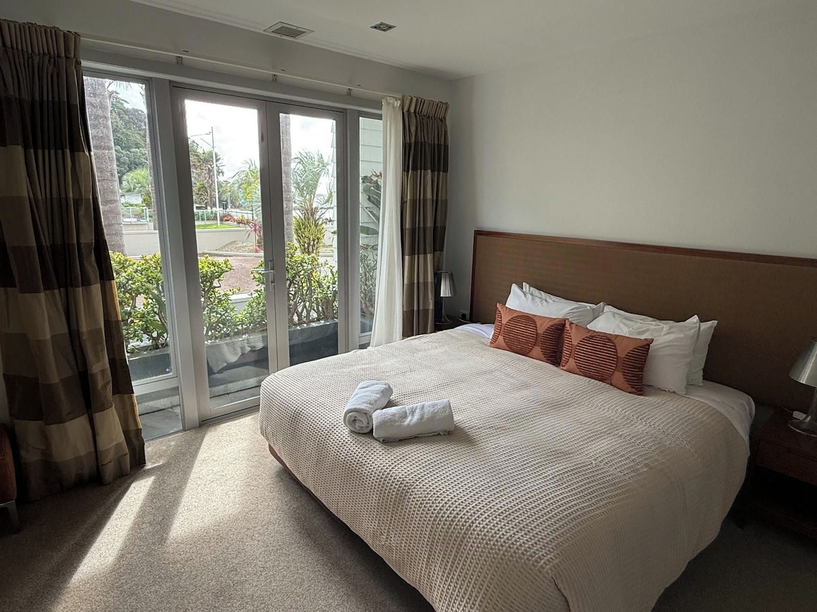 Habitación de hotel con una cama grande, vista por la ventana y una mesita de noche con lámpara.