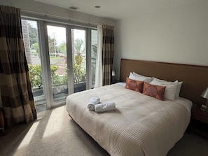 A hotel room with a large bed, a view through the window, and a nightstand with a lamp. - Paihia by the Sea (Paihia)