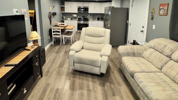 Un espacio habitable compacto con sofá, sillón reclinable, televisor y kitchenette.