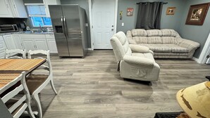 Una sala de estar moderna con un sofá, un sillón reclinable, una mesa de comedor con sillas, un refrigerador y una cocina con armarios y un microondas.