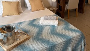 Ett hotellrum med en säng, ett matbord, en stol, en dekorativ väggdekoration och ett bricka med en vattenkokare och glas.