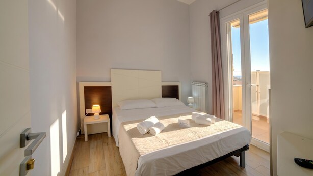 A hotel room with a bed, bedside tables, a lamp, a TV, and a balcony with curtains. - Archi Home - Apartment with Balcony in Central Lecce, Lecce, Italy (Lecce)