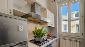 A kitchen with a stainless steel refrigerator, a gas stove, white cabinets, a window with a view, and a radiator. - Archi Home - Apartment with Balcony in Central Lecce, Lecce, Italy (Lecce)