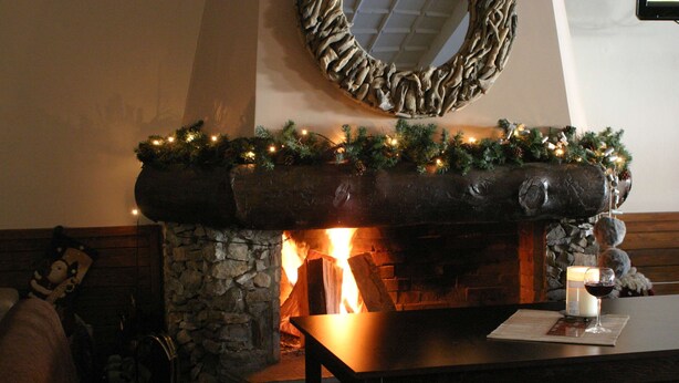 Une cheminée avec un manteau en pierre, une étagère décorée de guirlandes et de lumières, et une bougie posée sur une table devant.