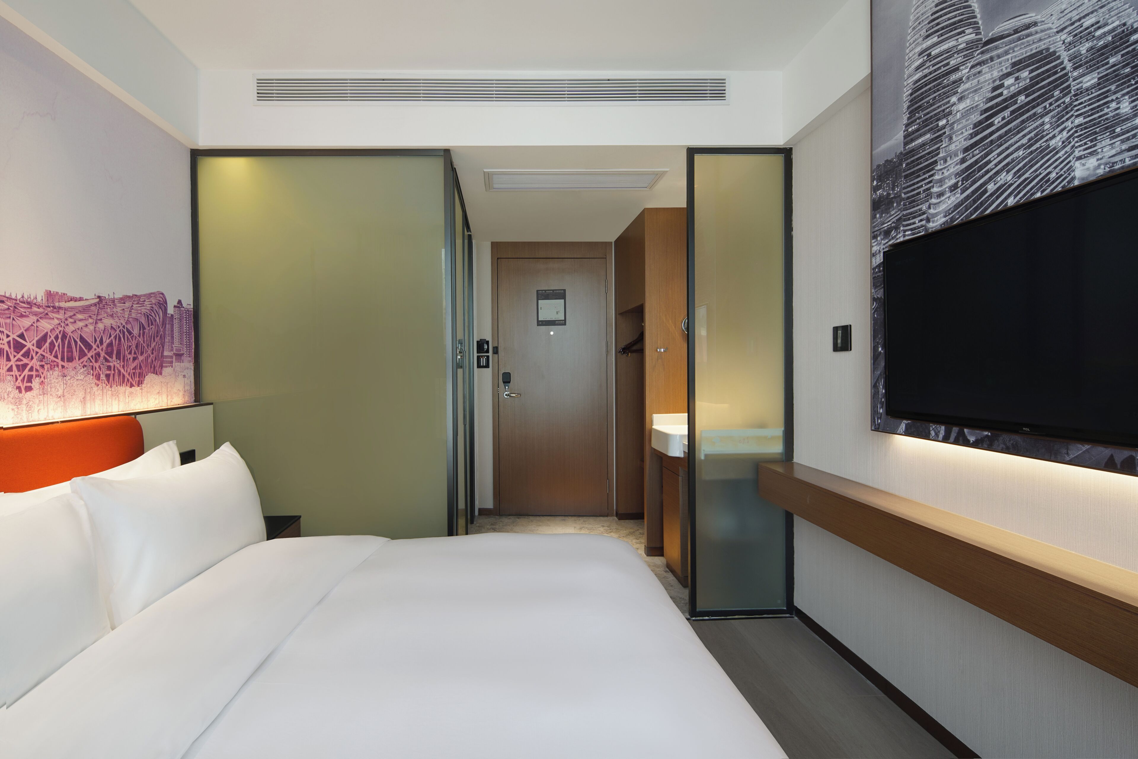 Ein Hotelzimmer mit Bett, Fernseher, Bad und einem zur anderen Kammer führenden Gang.